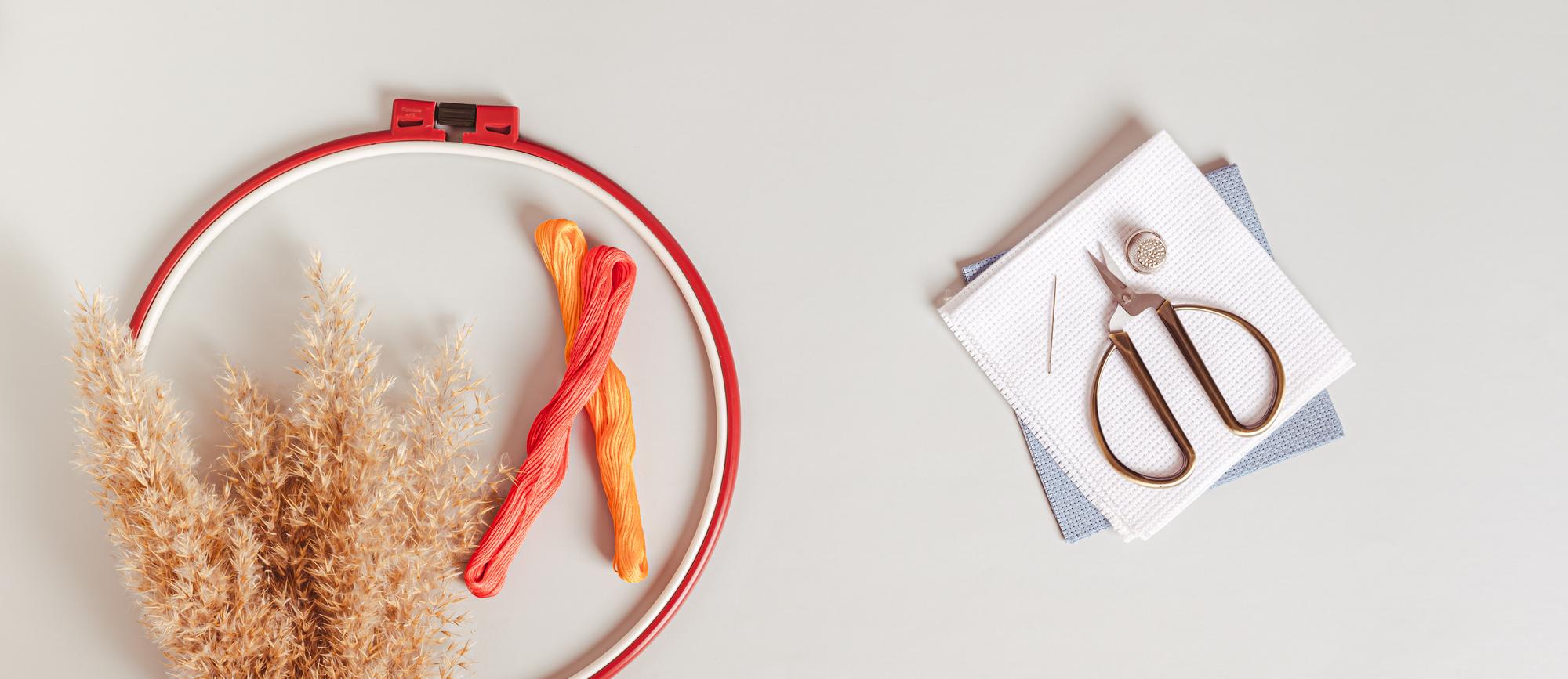 Flat-lay of modern hand embroidery hoop and threads on neutral background